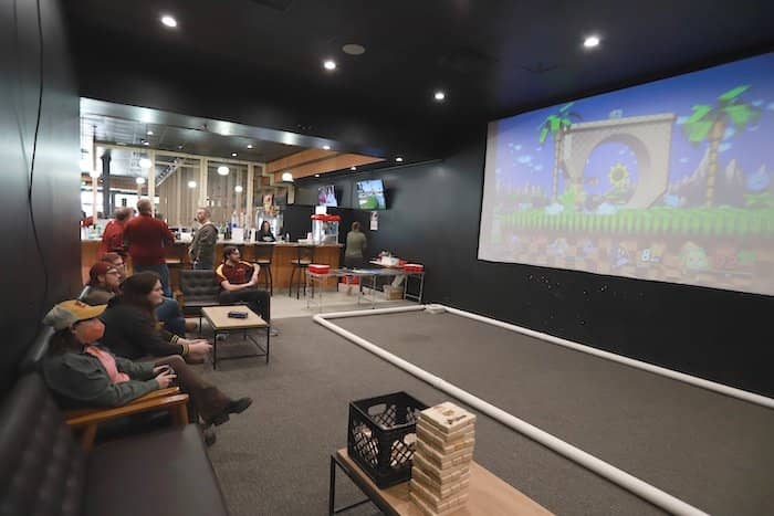 Staff members play and watch a video game on a big screen