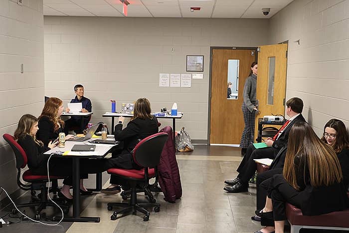 Students seated at tables and on benches in the hallway of Grawn Hall, some using laptops and cell phones.