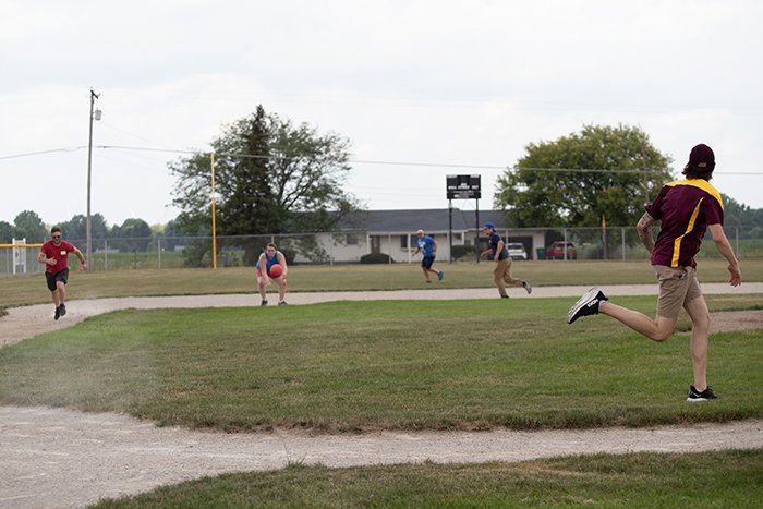 The kicker runs toward first while the third base player fields the ball.