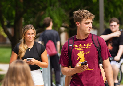 Two students walking around campus and looking around at a crowd while holding smartphones