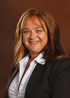 Professional headshot of Dr. Veronica Barone in white and black attire against a brown background.