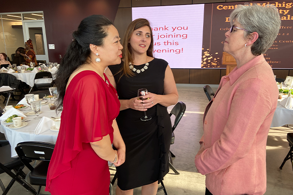 Three women in formal attire having a conversation among dining tables at Central Michigan University's Campus Diversity Symposium.