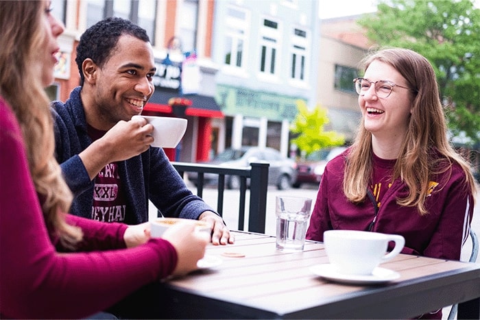 three students with coffee mugs sit at an outside table downtown