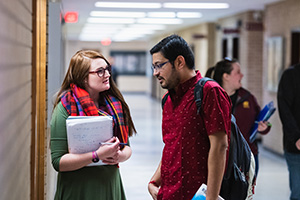 After leaving class, two mathematics graduate students, a woman and a man, stand in the hallway discussing assignments.
