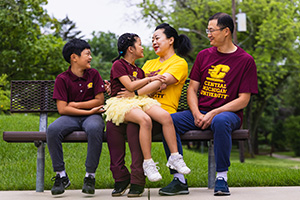A young Asian family talk together on a park bench.