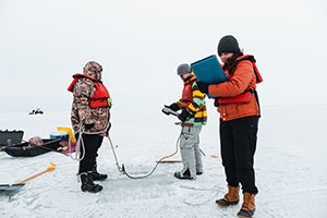 Three Central Michigan University biology students in warm winter gear take recordings on frozen Lake Huron