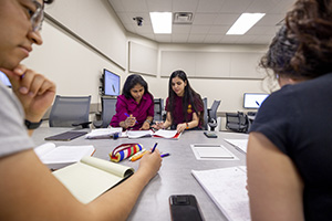 A group of three mathematics students, a male and two females, work with their mathematics professor in a large active learning classroom.