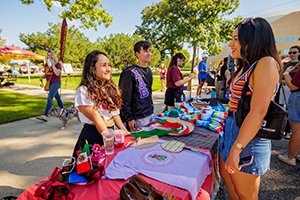 An interested student talks to a member of a CMU student organization standing behind a table during an outdoor campus life showcase.