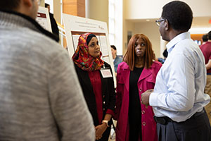 A group of presenters and students discuss a display of research projects in the hallway of the College of Health Professions at Central Michigan University.