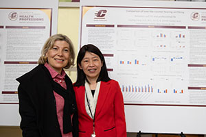 Two women stand in front of a display showcasing research done in the College of Health Professions at Central Michigan University.