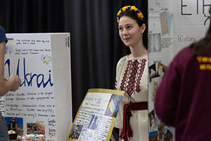 A young woman in traditional Ukrainian dress with flowers in her hair talks to students about the culture of her country.