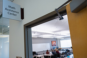 Photo of the entrance to the Math Assistance Center at Central Michigan University. Inside two students work with a peer tutor.