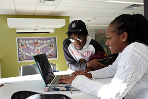 a man and woman leaning on a desk and looking at a laptop screen smiling
