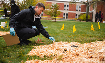 An anthropology student crouches down near a mock crime scene on campus to logging evidence.