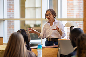 A woman in a white shirt standing in front of a group of people in a classroom.
