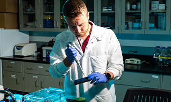 A student in a lab coat uses a diluter on a petri dish in a laboratory.
