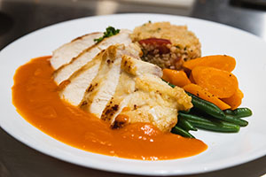 A round white plate with sweet potato puree, roasted turkey breast, steamed green beans and carrots and stuffing arranged artistically in a circle.