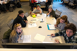 A group of students sit around a table with an interactive whiteboard at the end of it.