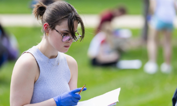 A student wearing blue latex gloves holding a pen and paper surveying a scene.