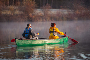 Two people navigate a river by canoe