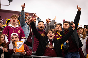 A group of Central Michigan University students huddle together and have their arms up in celebration posing for the photo