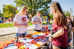A group of women wearing Central Michigan University shirts standing outside looking at a table with paper and other items.