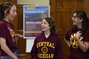 a group of people in CMU shirts face each other while smiling and having a conversation gesturing with their hands