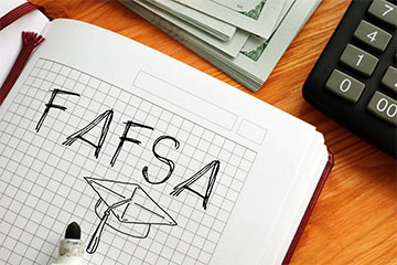 A notebook page with the word FAFSA written in black ink above a drawing of a graduation cap.