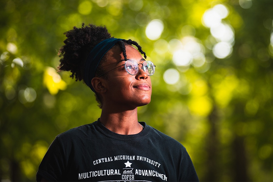 A student wearing a black Multicultural Advancement CMU t-shirt while looking into the distance.