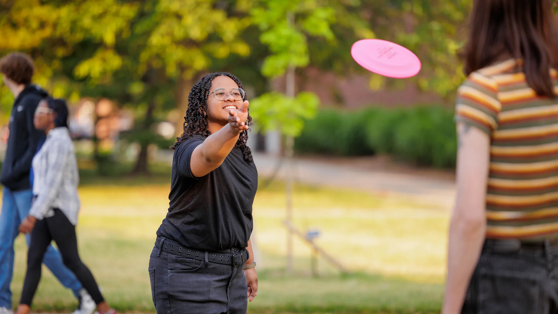 A student throwing a red frisbee on Central Michigan Universities campus in the summer, as green grass and trees surround.