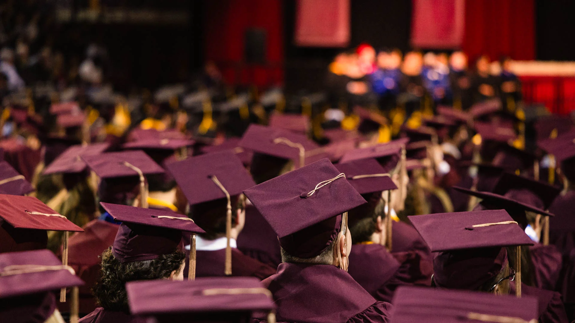sea of grad caps a large crowd of graduates wearing maroon caps and gowns stand together at commencement ceremonies