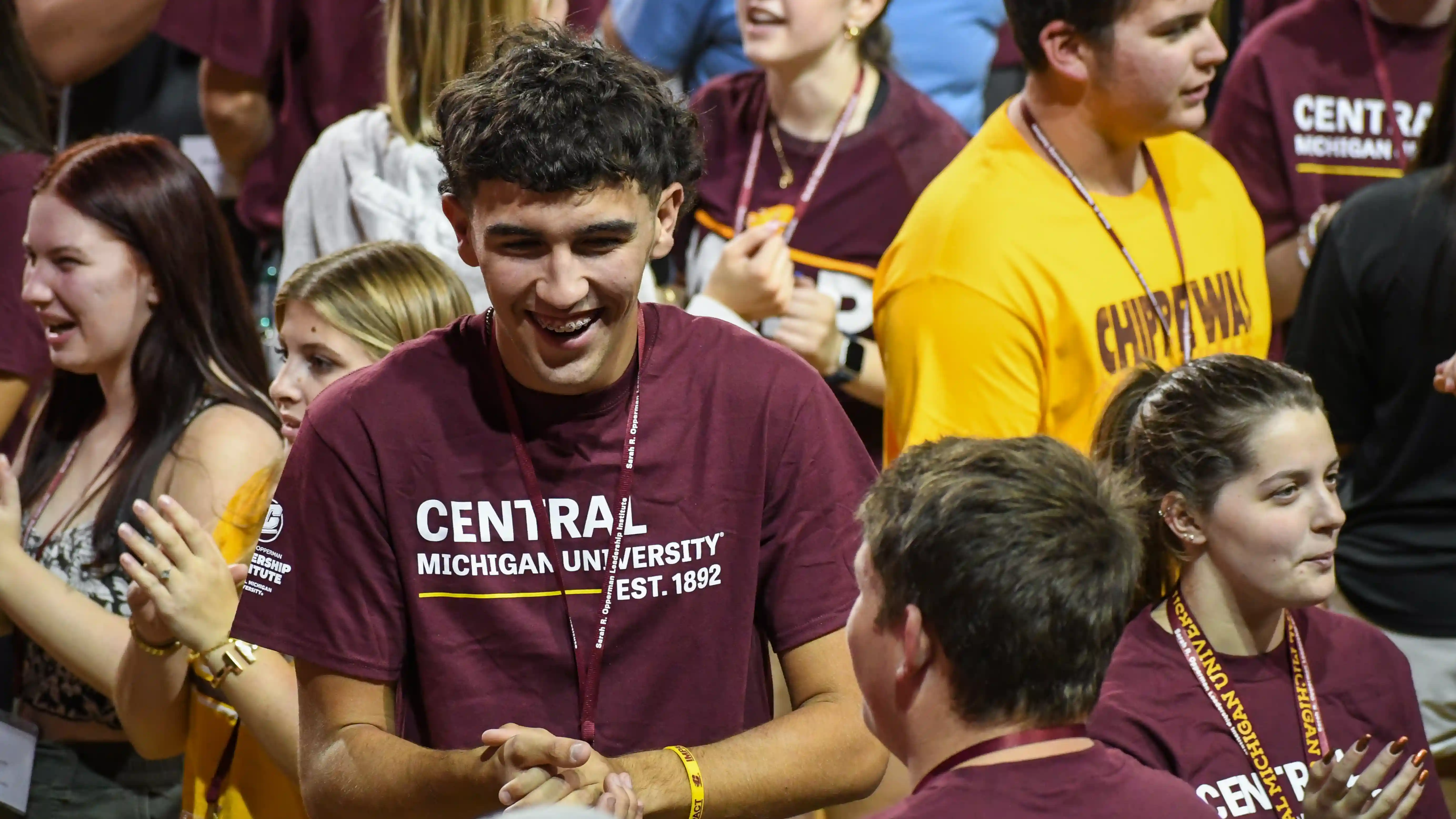 A group of students wearing maroon and gold t shirts that say Central Michigan University Est. 1892 while smiling at an event on campus.