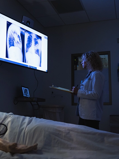 A female medical student wearing a white lab coat looks at x-ray images.