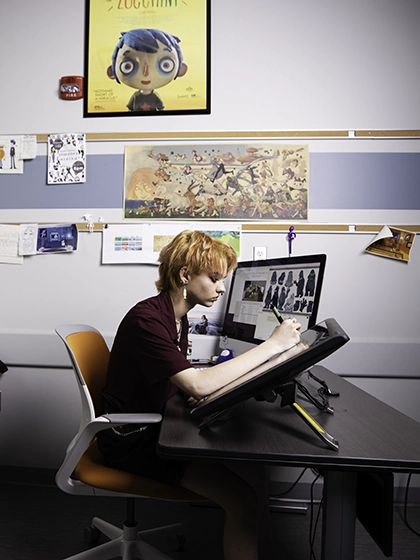 A student sits in an orange chair while working on a large monitor for an animation class.