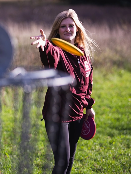 A student throws a disc golf disc into the goal on campus.