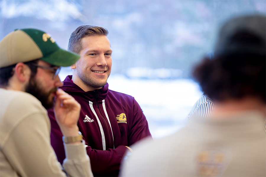 A man in a maroon jacket having a conversation with three other individuals indoors
