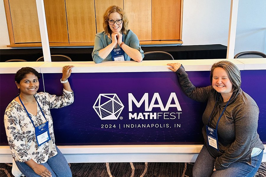 Three mathematics doctoral candidates smile at a Mathfest booth.