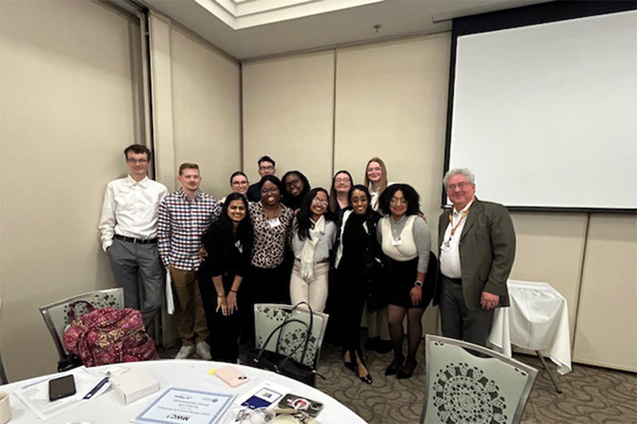 Faculty member stands with students at Midwest Collegiate Computing Conference.