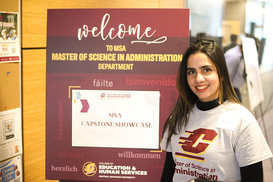 MSA student stands next to sign welcoming visitors to the MSA capstone showcase.