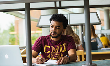 A student studies at a table with books and a laptop