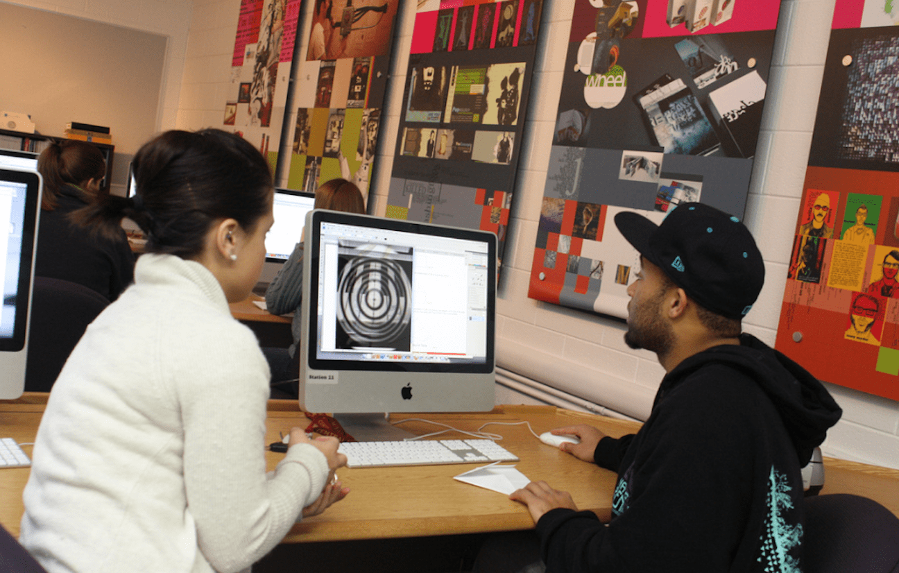 Two students sitting in a computer lab while looking at a design on a computer screen.