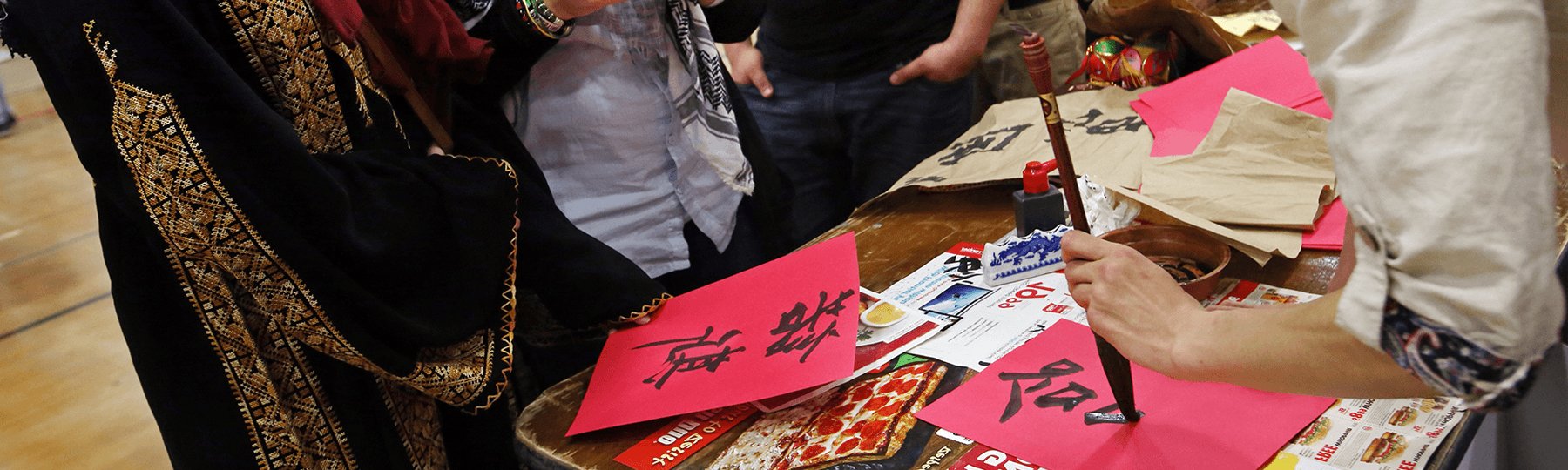 People hold calligraphy brushes and write words on red paper