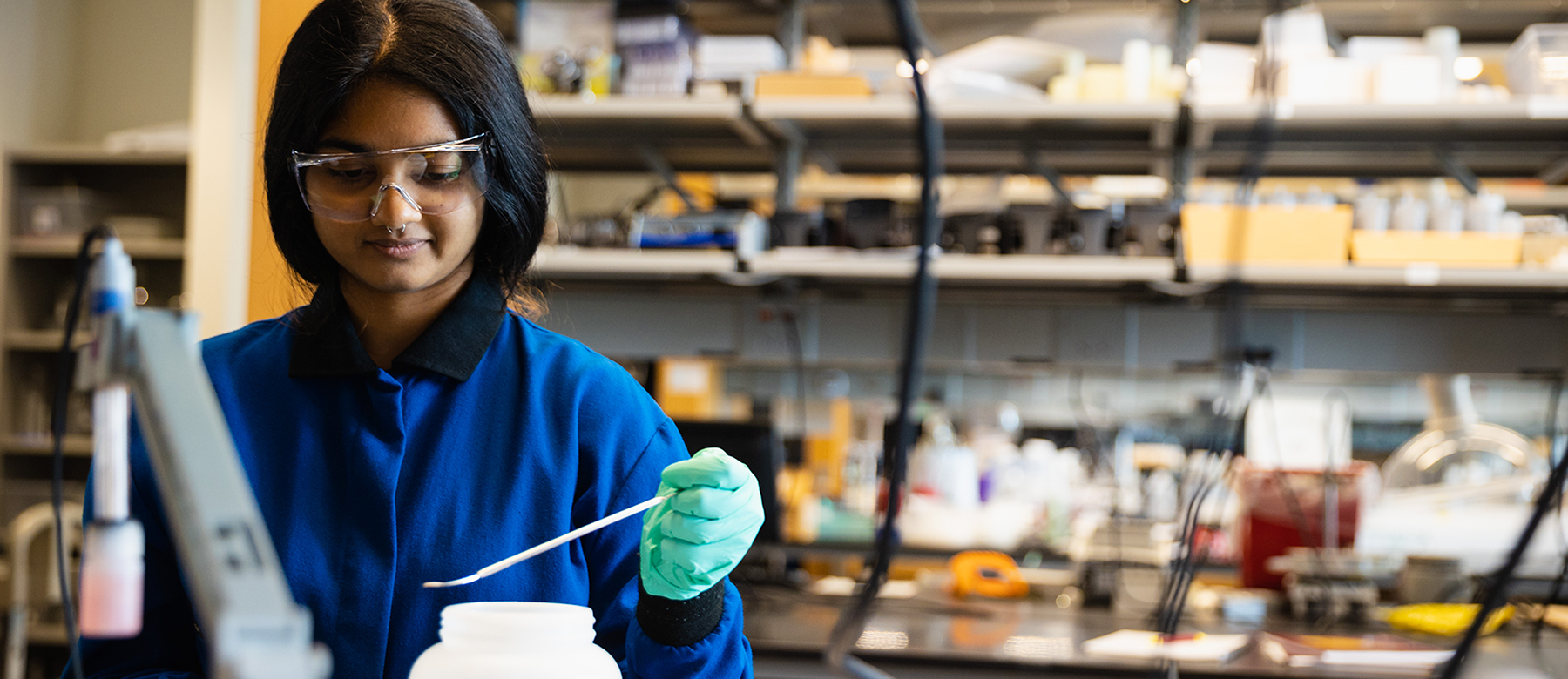 Female student in blue lab jacket scooping chemical substance for experiment