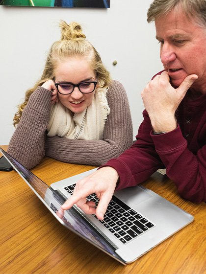 A professor and student collaborate with a laptop.