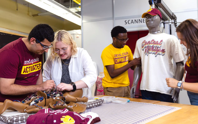 11137_Landing Page_635x397_StatBox_HND_RWR_IMD_fam1 Two people work on a small child-size robotic manikin with it's wire's exposed. In the background, two more students dress an adult-size manikin.