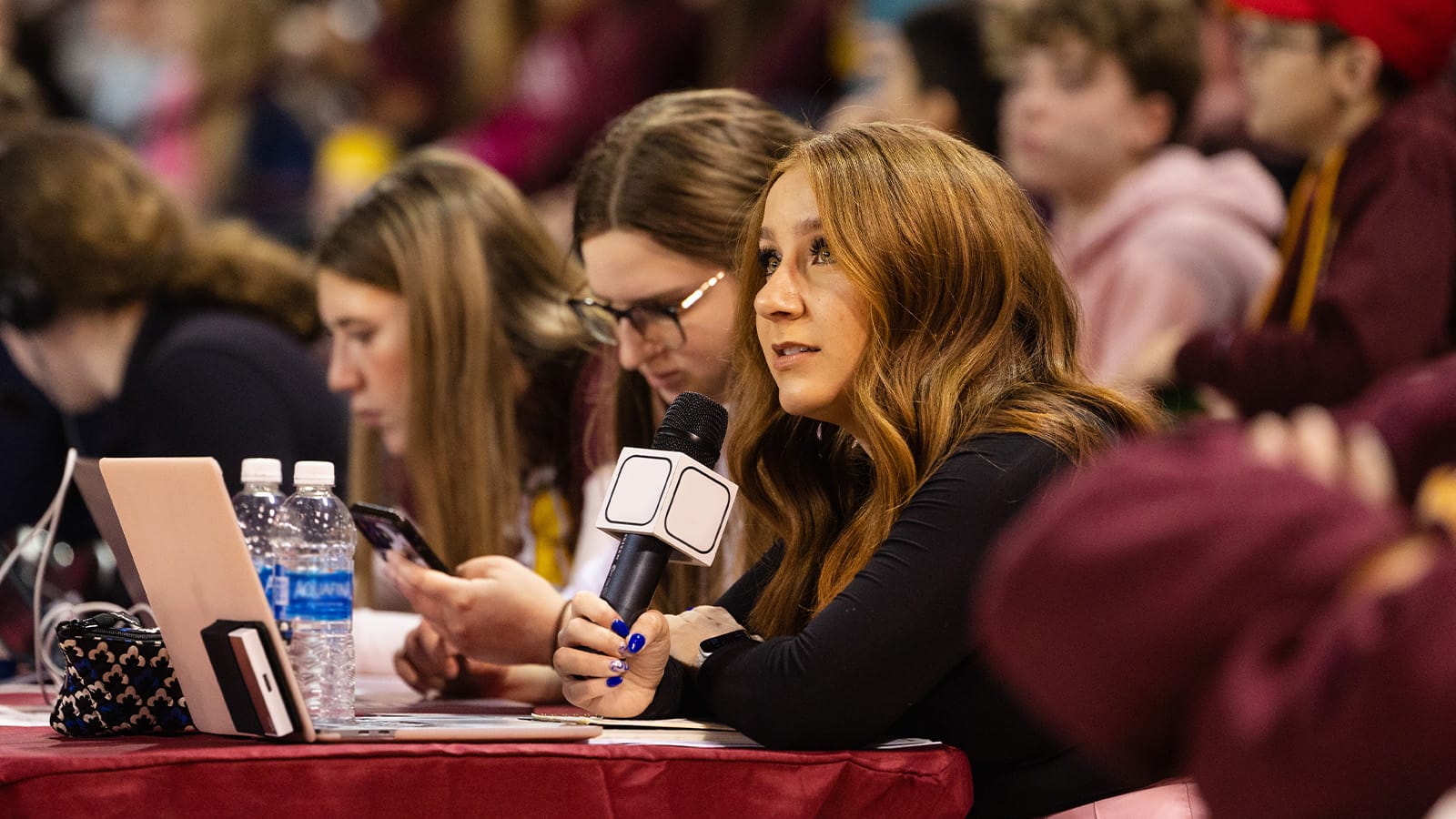 1600x900_Christiana Rosa_24-01-17 A CMU student sits at a sideline table at a basketball game, speaking into a microphone.