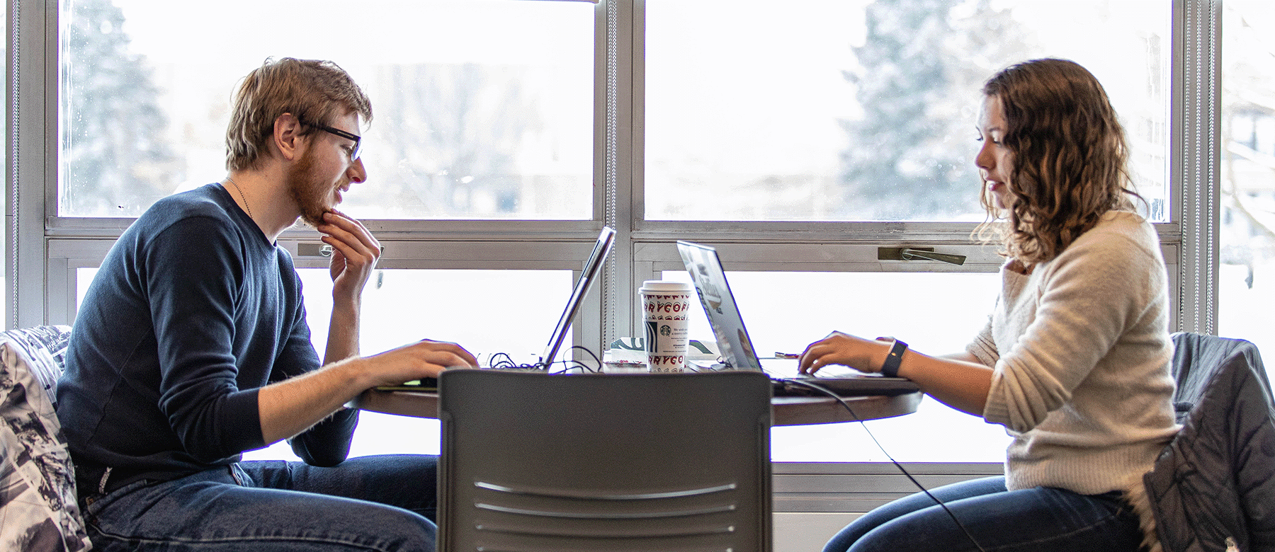 two people sitting at table with laptops