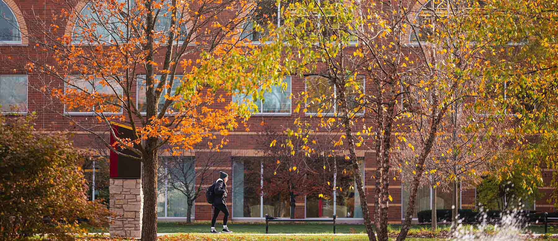 Student walking on campus surrounded by maroon and gold of fall trees