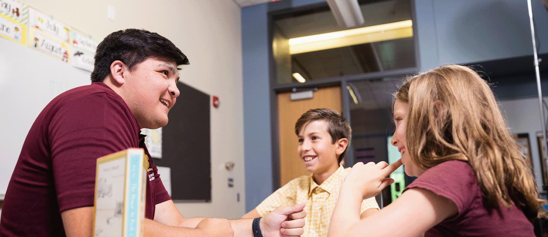 Student kneeling at desk of two children, all smiling