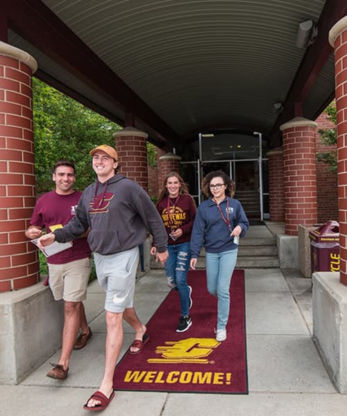 Four students walking out of residence hall wearing cmu gear.